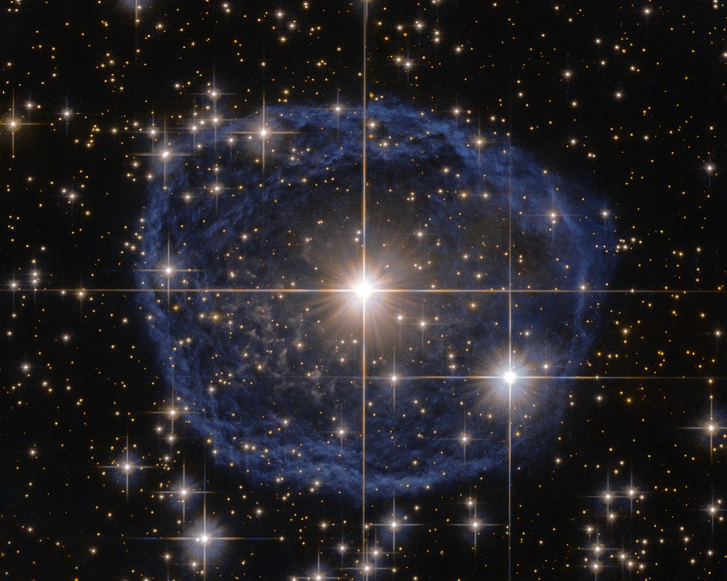 Sparkling at the centre of this beautiful NASA/ESA Hubble Space Telescope image is a Wolf–Rayet star known as WR 31a, located about 30 000 light-years away in the constellation of Carina (The Keel). The distinctive blue bubble appearing to encircle WR 31a, and its uncatalogued stellar sidekick, is a Wolf–Rayet nebula — an interstellar cloud of dust, hydrogen, helium and other gases. Created when speedy stellar winds interact with the outer layers of hydrogen ejected by Wolf–Rayet stars, these nebulae are frequently ring-shaped or spherical. The bubble — estimated to have formed around 20 000 years ago — is expanding at a rate of around 220 000 kilometres per hour! Unfortunately, the lifecycle of a Wolf–Rayet star is only a few hundred thousand years — the blink of an eye in cosmic terms. Despite beginning life with a mass at least 20 times that of the Sun, Wolf–Rayet stars typically lose half their mass in less than 100 000 years. And WR 31a is no exception to this case. It will, therefore, eventually end its life as a spectacular supernova, and the stellar material expelled from its explosion will later nourish a new generation of stars and planets.