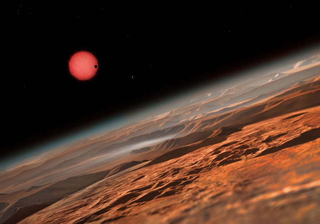 This artist’s impression shows an imagined view from close to one of the three planets orbiting an ultracool dwarf star just 40 light-years from Earth that were discovered using the TRAPPIST telescope at ESO’s La Silla Observatory. These worlds have sizes and temperatures similar to those of Venus and Earth and are the best targets found so far for the search for life outside the Solar System. They are the first planets ever discovered around such a tiny and dim star. In this view one of the inner planets is seen in transit across the disc of its tiny and dim parent star.