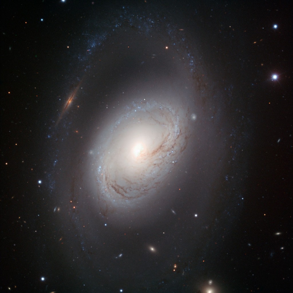 Not all spiral galaxies have to be picture-perfect to be striking. Messier 96, also known as NGC 3368, is a case in point: its core is displaced from the centre, its gas and dust are distributed asymmetrically and its spiral arms are ill-defined. But this portrait, taken with the FORS1 instrument on ESO’s Very Large Telescope, shows that imperfection is beauty in Messier 96. The galaxy's core is compact but glowing, and the dark dust lanes around it move in a delicate swirl towards the nucleus. And the spiral arms, patchy rings of young blue stars, are like necklaces of blue pearls. &nbsp; Messier 96 lies in the constellation of Leo (The Lion). It is the largest galaxy in the Leo I group of galaxies; including its outermost spiral arms, it spans some 100 000 light-years in diameter — about the size of our Milky Way. Its graceful imperfections likely result from the gravitational pull of other members in the group, or are perhaps due to past galactic encounters.&nbsp; A multitude of background galaxies peers through the dusty spiral. Perhaps the most striking of these objects is an edge-on galaxy that — because of a chance alignment — appears to interrupt the outermost spiral arm to the upper left of Messier 96's core. This image was processed by ESO using the observational data found by Oleg Maliy from Ukraine, who participated in ESO's Hidden Treasures 2010 astrophotography competition [1], organised in October–November 2010, for everyone who enjoys making beautiful images of the night sky using astronomical data obtained with professional telescopes. The image was made with data taken at visible and infrared wavelengths through B, V, and I filters.&nbsp; Notes [1] ESO’s Hidden Treasures 2010 competition gave amateur astronomers the opportunity to search through ESO’s vast archives of astronomical data, hoping to find a well-hidden gem that needed polishing by the entrants. To find out more about Hidden Treasures, visit https://www.eso.org/public/outreach/hiddentr