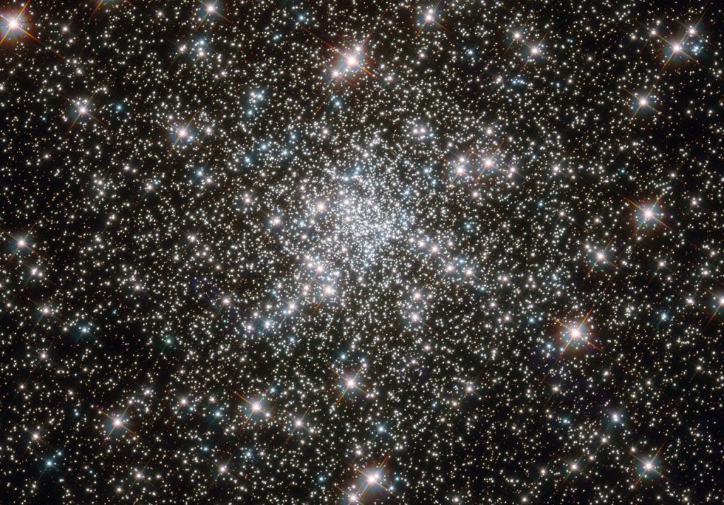 Looking like a hoard of gems fit for an emperor’s collection, this deep sky object called NGC 6752 is in fact far more worthy of admiration. It is a globular cluster, and at over 10 billion years old is one the most ancient collections of stars known. It has been blazing for well over twice as long long as our Solar System has existed. NGC 6752 contains a high number of “blue straggler” stars, some of which are visible in this image. These stars display characteristics of stars younger than their neighbours, despite models suggesting that most of the stars within globular clusters should have formed at approximately the same time. Their origin is therefore something of a mystery. Studies of NGC 6752 may shed light on this situation. It appears that a very high number — up to 38% — of the stars within its core region are binary systems. Collisions between stars in this turbulent area could produce the blue stragglers that are so prevalent. Lying 13 000 light-years distant, NGC 6752 is far beyond our reach, yet the clarity of Hubble’s images brings it tantalisingly close.
